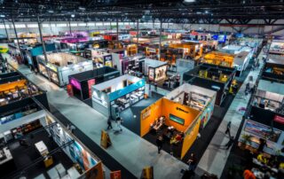 A vibrant exhibition hall with colorful booths and people moving and interacting, capturing the energy of the event