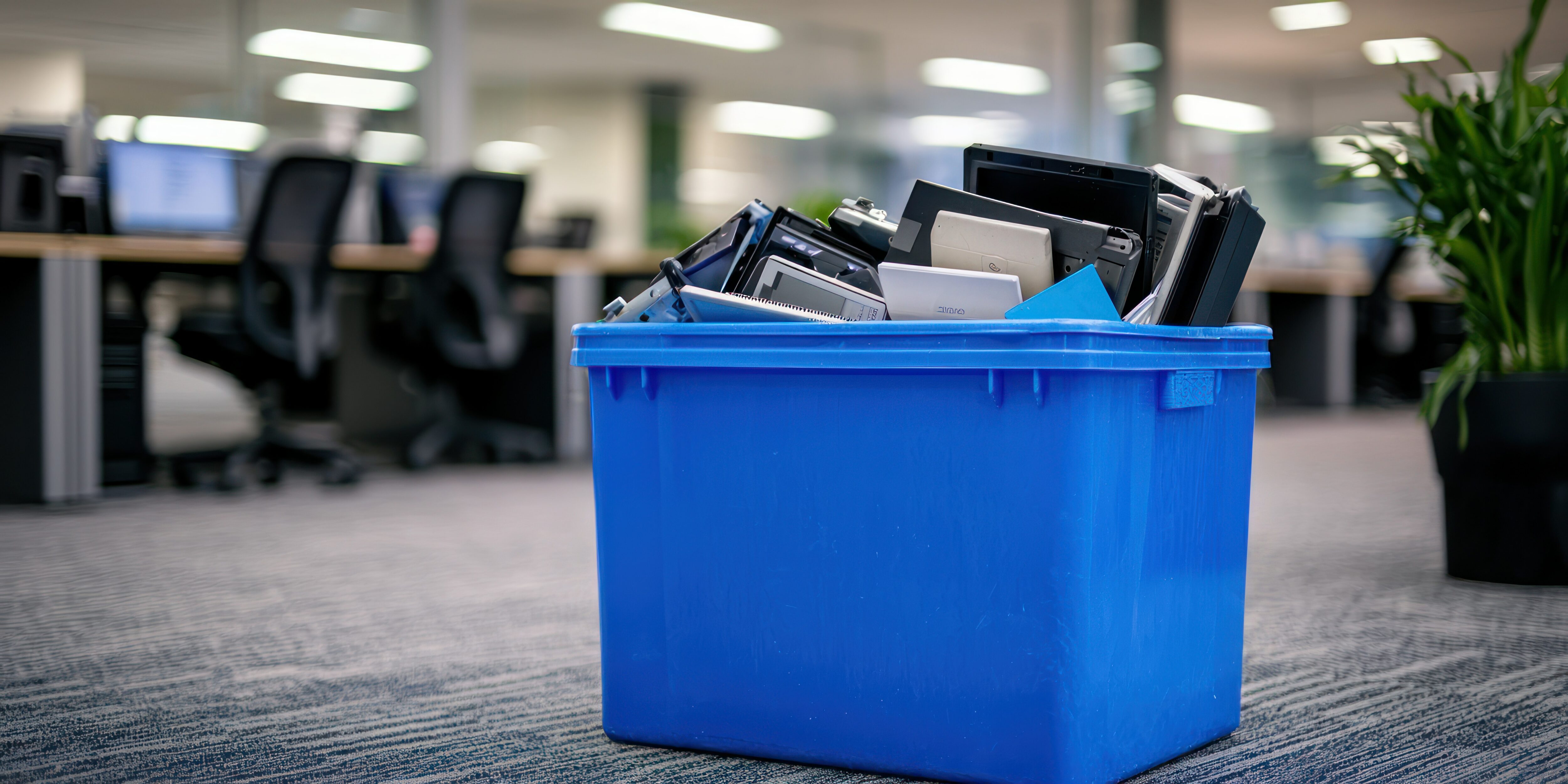 A blue e-waste bin in a corporate office, filled with outdated electronic devices.