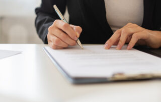 Wide view closeup image of a businesswoman signing a document or lease agreement in a folder.