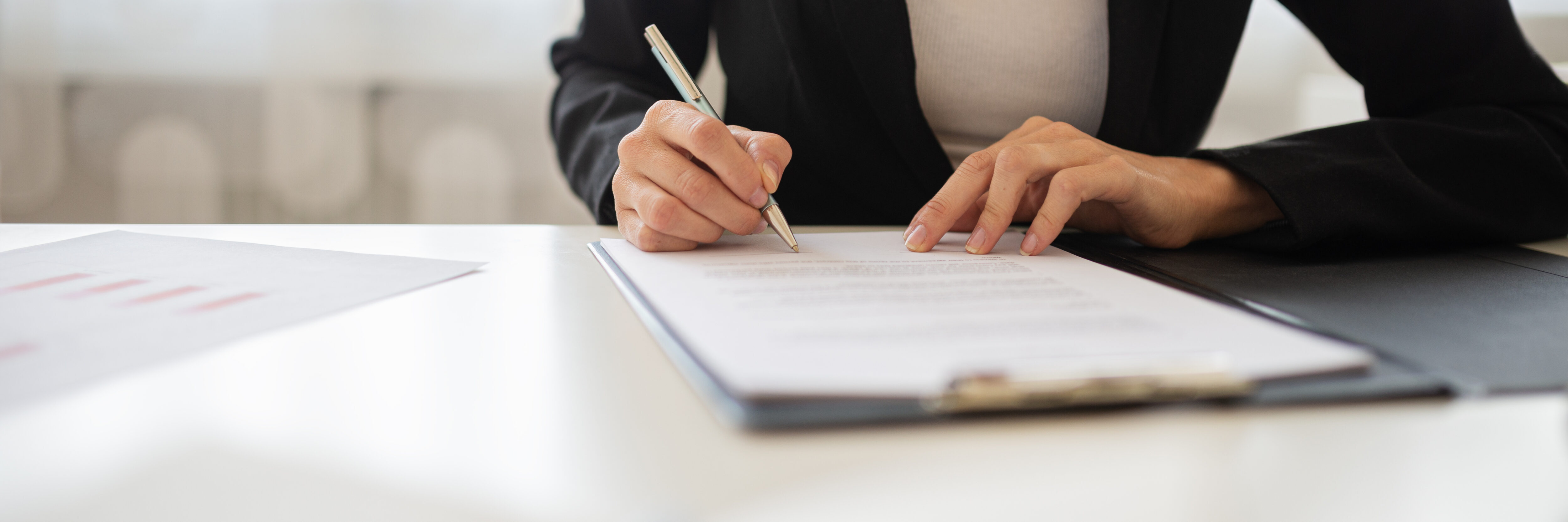 Wide view closeup image of a businesswoman signing a document or lease agreement in a folder.