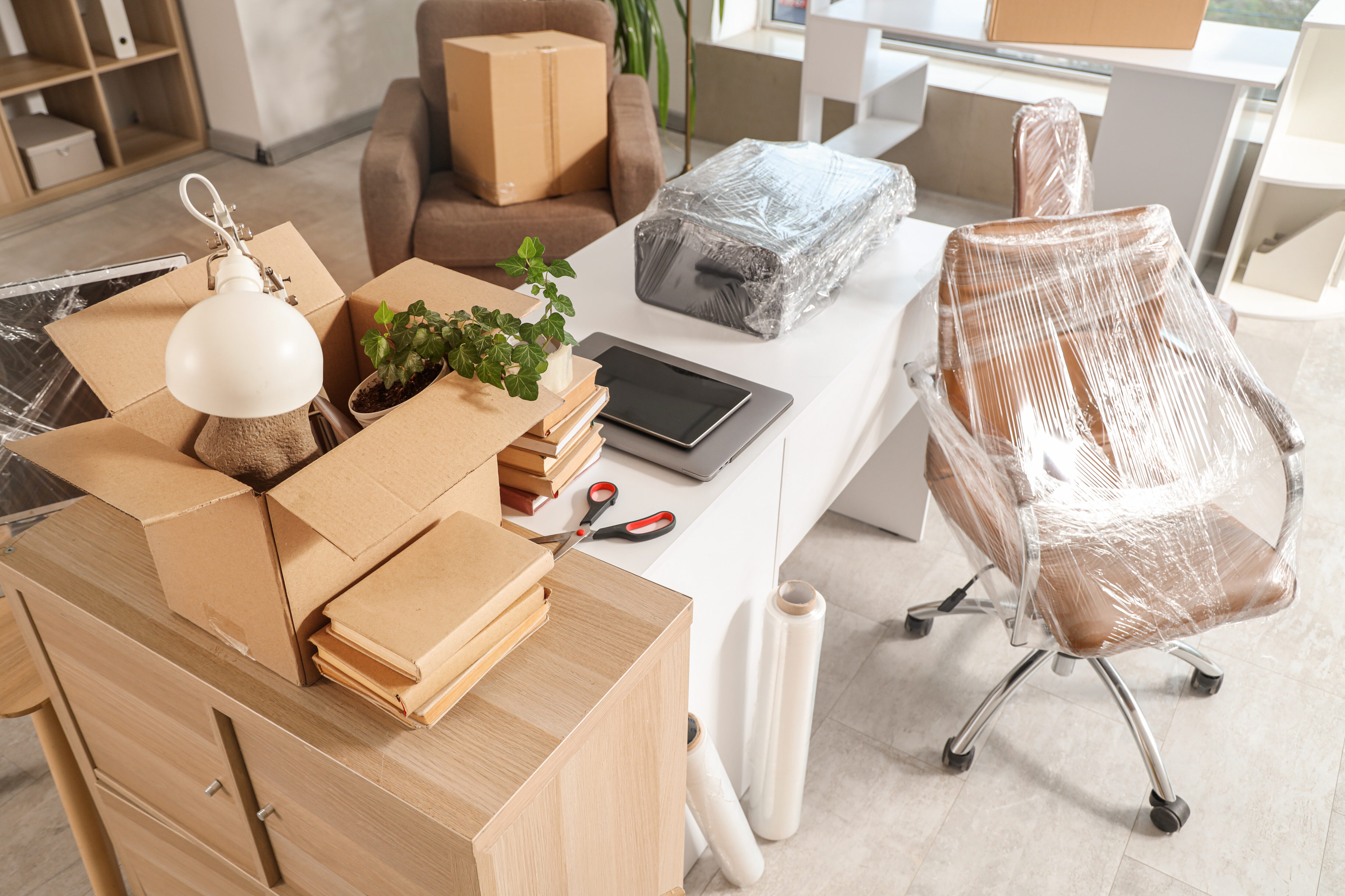 Interior of office with desk, boxes and wrapped chairs in stretch film on moving day